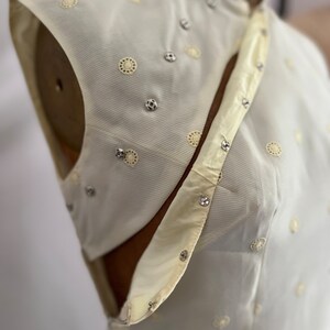 Pode incluir: Um top branco sem mangas com gola mandarim e um design decorativo de pequenos c&iacute;rculos e strass.