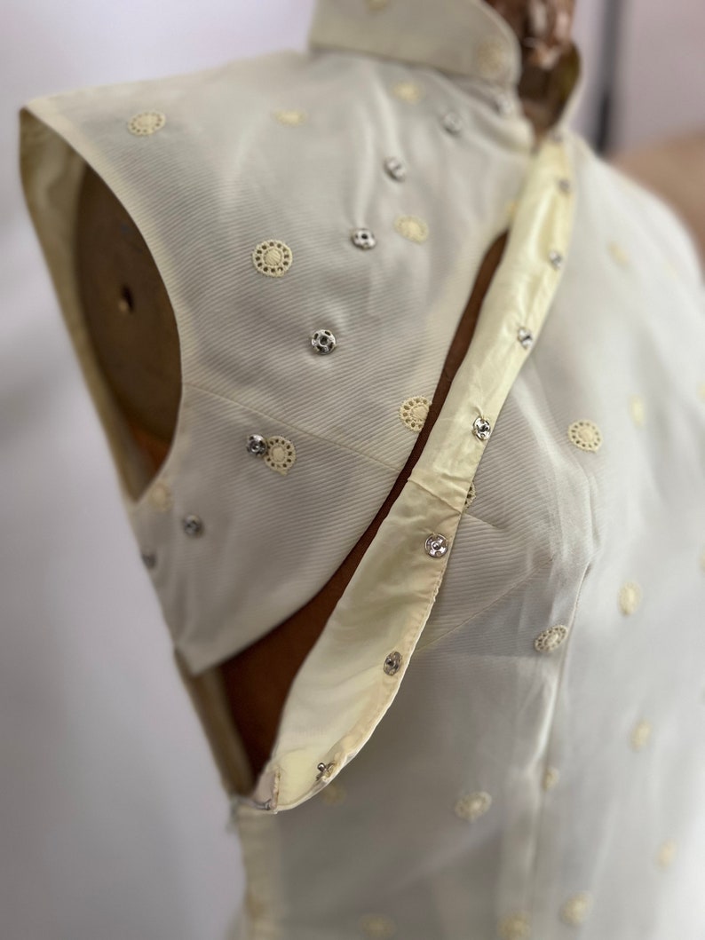 Pode incluir: Um top branco sem mangas com gola mandarim e um design decorativo de pequenos c&iacute;rculos e strass.