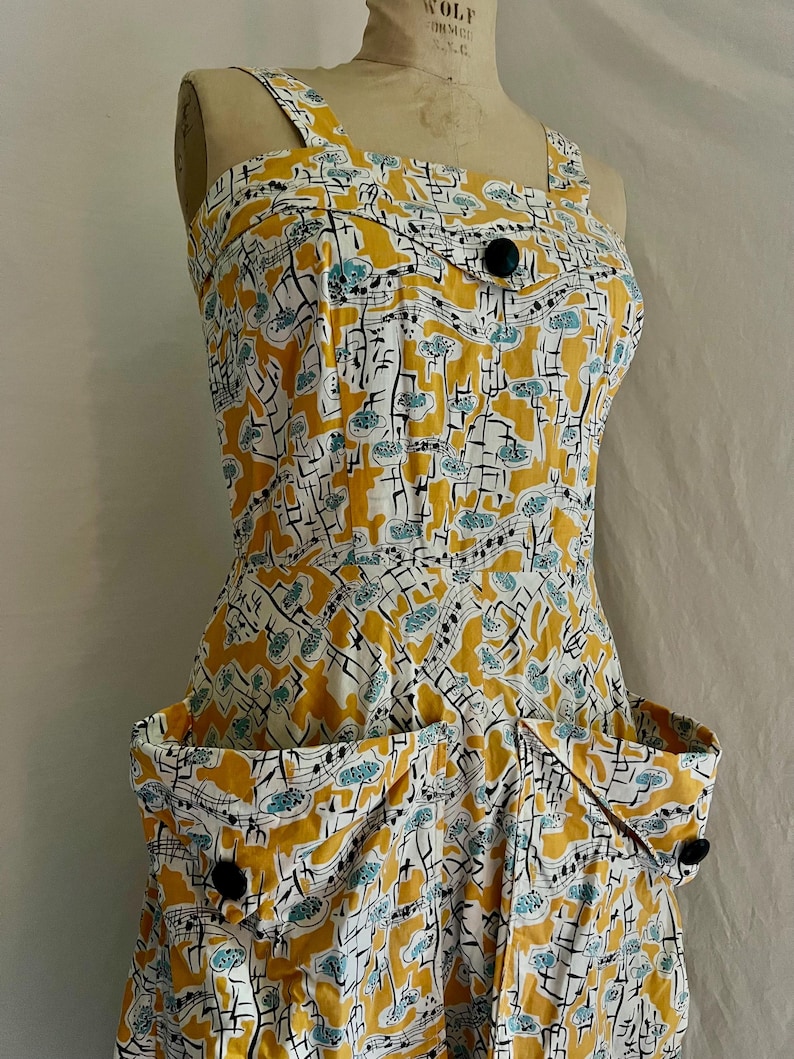 K&ouml;nnte beinhalten: Vintage Kleid mit gelbem, wei&szlig;em und schwarzem Muster. Es hat ein einzigartiges Muster aus Noten und abstrakten Formen. Quadratischer Ausschnitt, zwei gro&szlig;e Taschen und schwarze Kn&ouml;pfe. Ma&szlig;e sind nicht verf&uuml;gbar.