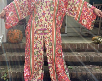 May include: A long-sleeved, wide-legged jumpsuit with a floral print in shades of orange, pink, green, and white. The jumpsuit has a relaxed fit and a round neckline.