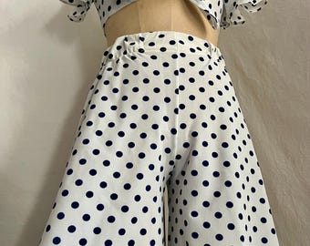 May include: A white and navy blue polka dot crop top and wide-leg pants set. The top has a tie at the front and short, ruffled sleeves.