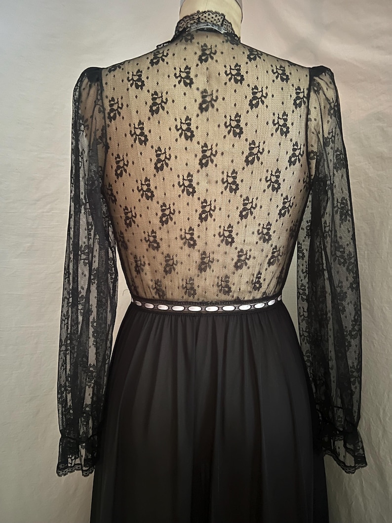 May include: Black vintage dress with a high neckline and long sleeves. The bodice is sheer black lace with a floral pattern over a nude lining. The waist is accented with a white ribbon and the skirt is a solid black fabric.