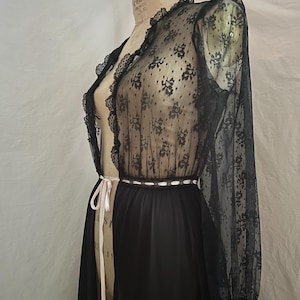 May include: Black lace robe with floral patterns and long sleeves. The robe has a sheer design with a black skirt and a white ribbon belt. The robe is displayed on a mannequin.