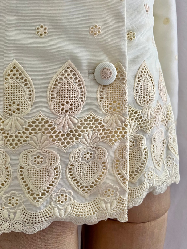 Pode incluir: Uma jaqueta branca bordada com uma bainha festonada e um fecho de bot&atilde;o &uacute;nico. O bordado apresenta um delicado padr&atilde;o floral e um design de cora&ccedil;&atilde;o.