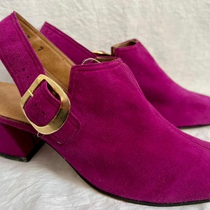 May include: A pair of magenta suede slingback shoes with a gold-colored buckle. The shoes have a block heel and a rounded toe. The size is 7.