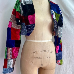 May include: A cropped patchwork jacket with long sleeves. The jacket is made of velvet and features a variety of colors and patterns, including red, blue, green, pink, and black.