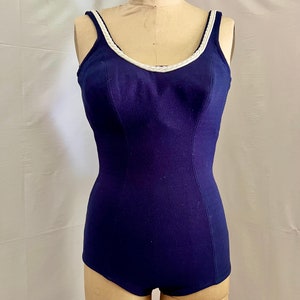 May include: A navy blue swimsuit with a white trim around the neckline. The swimsuit has a fitted bodice and a high leg cut.