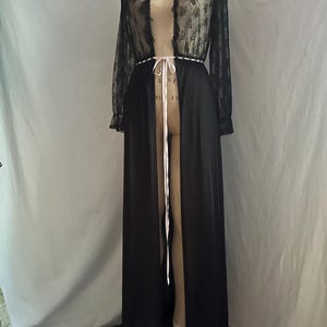 May include: A long, black robe with a sheer, floral lace top and sleeves. The robe has a high collar and a white ribbon tie at the waist. The robe is displayed on a mannequin.
