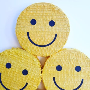 May include: Three yellow smiley face pinatas with black eyes and mouths. The pinatas are made of tissue paper and are a fun party decoration.