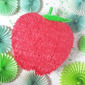May include: A red apple-shaped pinata with green paper streamers. The pinata is surrounded by green and light blue paper decorations.
