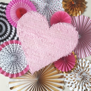 May include: A pink heart-shaped pinata surrounded by paper fans in various colours and patterns, including black and white, gold, and pink.