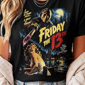 May include: A black t-shirt featuring a graphic print of the Friday the 13th movie poster. The design shows a masked figure holding a machete above a woman, with text that reads A Camp of Young Folks... A Night of Terror! and Pray You Never Come to Camp Crystal Lake!