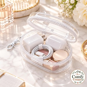 May include: A clear, oval-shaped zipped pouch containing a white power adapter, a white charging cable, a white wireless earbud case, and a small round gold-toned compact. The pouch features a white zip and a silver-toned metal lobster clasp.