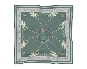 May include: A square scarf in muted sage green featuring a central crest with a serpent emblem and the text Slytherin. The design includes white floral accents in the corners, a decorative border with a geometric pattern, and the letter S.