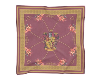May include: A square scarf in a deep maroon color featuring a central Gryffindor crest with a lion, surrounded by orange floral accents and gold geometric border patterns. The letter G is printed in each corner of the maroon fabric field.