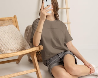 May include: A taupe short-sleeved t-shirt featuring small, dark text printed on the chest that reads modeled after figure sketches. The shirt has a crew neckline and a relaxed fit, paired with dark gray denim shorts.