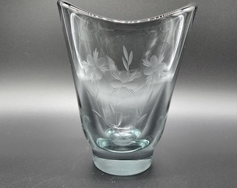 Op de afbeelding: Een vaas van helder glas met een uitlopende, gebogen rand en een dikke voet. Het buitenoppervlak is voorzien van delicate, gegraveerde bloemmotieven, waaronder bloesems en slanke bladeren, wat zorgt voor een subtiel ontwerp.
