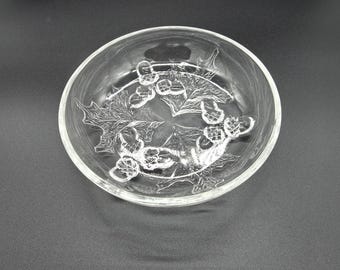 Op de afbeelding: Een heldere glazen kom met een reliëfontwerp van hulstbladeren en bessen op de binnenbodem. De ronde schaal heeft gladde, afgeronde randen en een transparante afwerking, waardoor het gedetailleerde botanische patroon in het glas zichtbaar is.