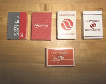 Op de afbeelding: Vijf rechthoekige kaartspellen met de branding van Northwest Airlines en Northwest Orient. De doosjes zijn rood, wit en grijs, met logo's en tekst waaronder 'Northwest Airlines', 'Northwest Orient' en 'The Only Way to Fly'.