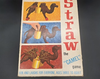 Op de afbeelding: Een rechthoekige bordspeldoos met de titel The Last Straw the Camel game. De hoes bevat drie illustraties van een bruine kameel met een gele container op de rug, die het spel met stokjes toont. Tekst bevat: Fun and laughs for everyone.
