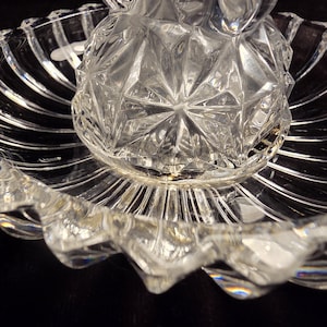 May include: A clear glass serving dish featuring a central raised section with a geometric diamond-cut pattern, surrounded by a wide, shallow bowl with a scalloped edge and radiating vertical fluted lines throughout the entire piece.