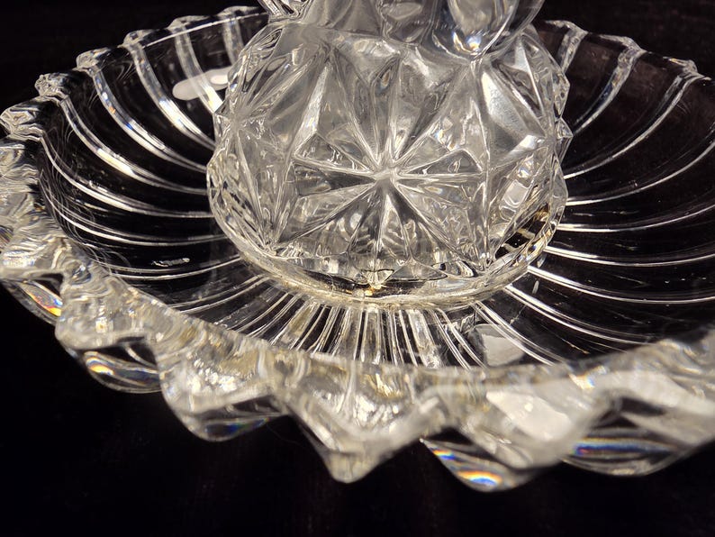May include: A clear glass serving dish featuring a central raised section with a geometric diamond-cut pattern, surrounded by a wide, shallow bowl with a scalloped edge and radiating vertical fluted lines throughout the entire piece.