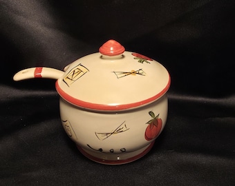 Op de afbeelding: Een crèmekleurige keramische pot met bijpassend deksel en een enkele handgreep aan de zijkant. De buitenkant is voorzien van handgeschilderde rode tomatenillustraties, zwarte lijntekeningen van pasta en een rode rand langs de bovenkant.