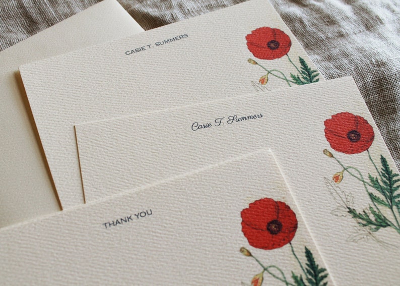May include: Set of three blank stationery cards with a floral design. The cards are cream colored with a subtle texture. Each card features a red poppy flower with green leaves and stems. The top card has the name "Cassie T. Summers" printed in black. The middle card has the name "Cassie T. Summers" printed in black cursive. The bottom card has the words "Thank You" printed in black.