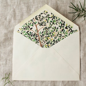 May include: A white envelope with a green and white floral pattern on the inside flap. The envelope is lying flat on a beige linen surface.