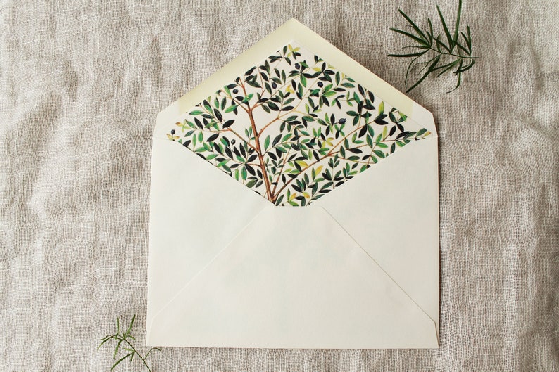 May include: A white envelope with a green and white floral pattern on the inside flap. The envelope is lying flat on a beige linen surface.