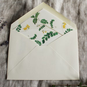 May include: A white envelope with a floral pattern on the inside flap. The pattern features green leaves and yellow flowers.