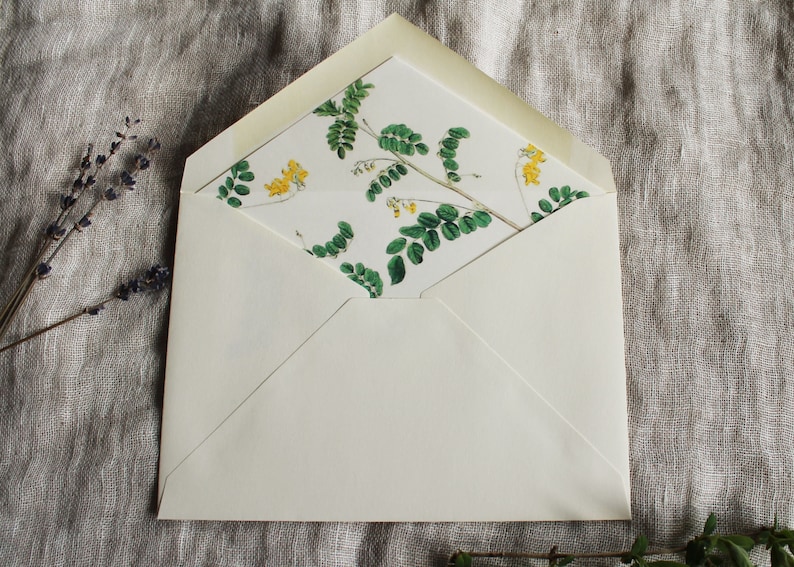 May include: A white envelope with a floral pattern on the inside flap. The pattern features green leaves and yellow flowers.