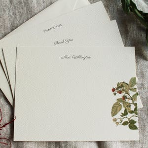 May include: A set of white stationery cards with a floral design featuring a green raspberry branch with red berries. The cards have the text "Thank You" and "Nica Wellington" printed on them.