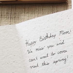 May include: A handwritten birthday card with the text "Happy Birthday Mom! We miss you and can't wait to come visit this spring!"