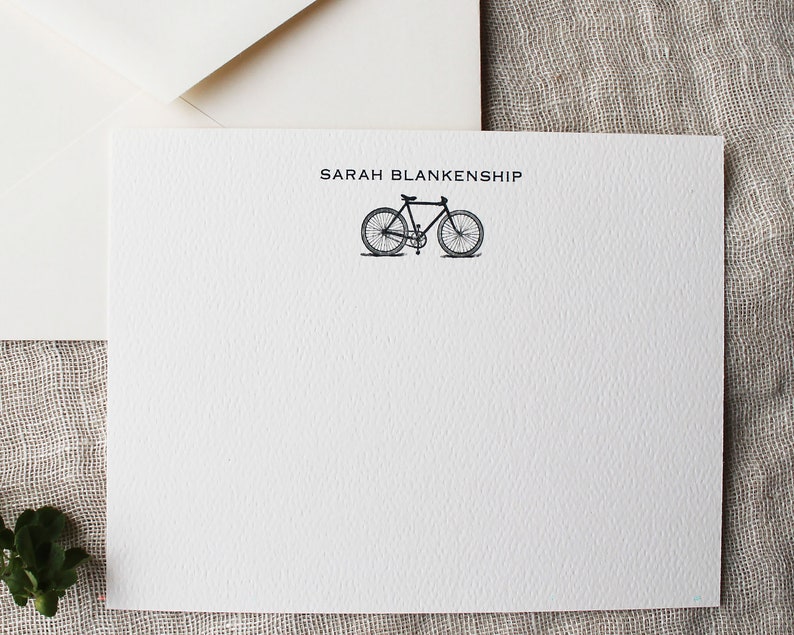 May include: White stationery card with the name "SARAH BLANKENSHIP" printed in black at the top. A black and white illustration of a bicycle is centered below the name.