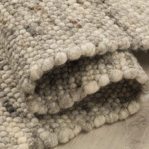 Könnte beinhalten: Ein dicker, handgetufteter Wollteppich mit einer dichten, strukturierten Oberfläche aus einzelnen gefilzten Kugeln. Der Teppich zeigt eine neutrale Farbpalette aus Creme-, Beige-, Hellgrau- und Dunkelbrauntönen in einem dezenten Muster.