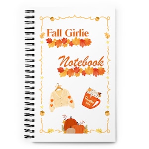 Puede incluir: Un cuaderno de espiral con portada blanca que presenta el texto Fall Girlie Notebook en naranja. El diseño incluye ilustraciones de hojas de otoño naranjas y rojas, un cárdigan color crema con patrones de corazones, una taza de pumpkin spice y calabazas.