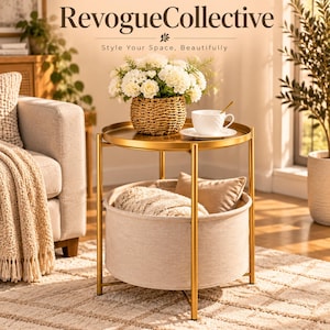 May include: A round gold metal side table with a tray top and a lower beige fabric storage basket. The table holds a woven basket with white flowers, a white teacup on a saucer, and a beige pillow inside the lower fabric storage compartment.