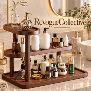 May include: A three-tiered dark wood bathroom organizer shelf holding various skincare bottles, jars, and makeup brushes. The text RevogueCollective is visible in the background. The organizer features rounded rectangular trays and cylindrical supports.
