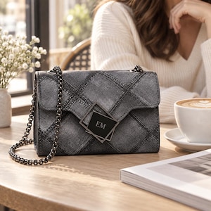 Puede incluir: Un bolso de mano de mezclilla gris carbón con un patrón de diamantes acolchado y una correa de cadena de metal oscuro. La solapa frontal está asegurada con un cierre metálico cuadrado que muestra las letras EM en una fuente clara y centrada.