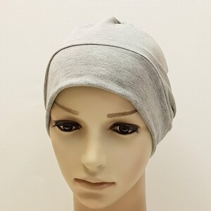 May include: A light gray beanie hat made of soft fabric. The hat is designed with a folded brim and a rounded crown. The beanie is shown on a mannequin head against a plain white background. This hat is suitable for casual wear.