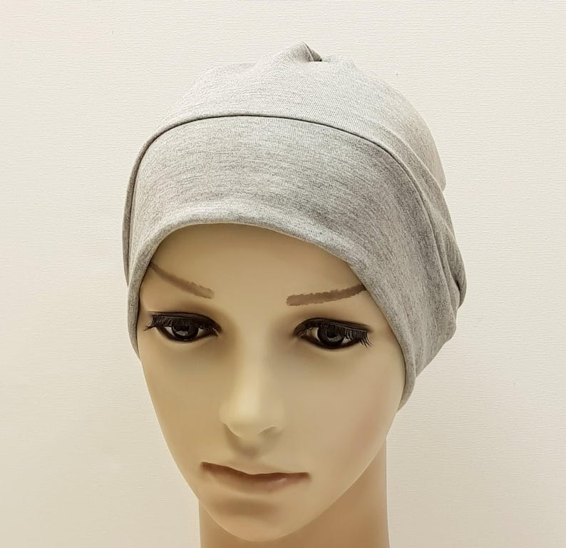 May include: A light gray beanie hat made of soft fabric. The hat is designed with a folded brim and a rounded crown. The beanie is shown on a mannequin head against a plain white background. This hat is suitable for casual wear.