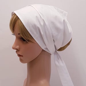 May include: A white headscarf, tied at the back of the neck, is shown on a mannequin. The head covering is made of a smooth, opaque fabric. The scarf is a solid white colour and is neatly folded and tied.