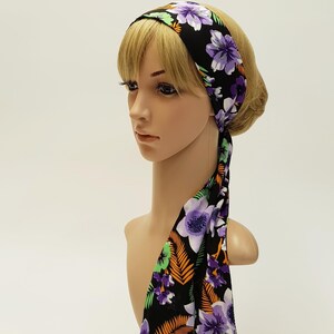 May include: A black headband with a floral pattern featuring purple, white, and green flowers and orange leaves. The headband is tied at the back, with the ends hanging down. The headband is on a mannequin head.