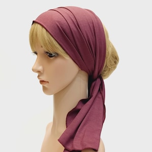 May include: A burgundy headscarf, tied at the back, is draped over a mannequin's head. The fabric is soft and appears to be a jersey knit. The head covering is a solid colour with a simple design, suitable for various occasions.