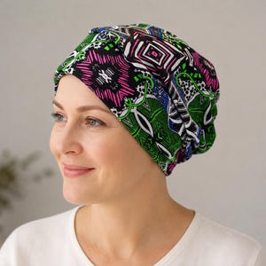 May include: A slouchy beanie hat featuring a vibrant, multi-coloured geometric and floral pattern in shades of bright pink, lime green, blue, black, and white. The fabric has a soft, gathered texture that creates a relaxed fit around the head.
