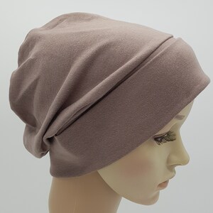 May include: A soft, brown beanie hat made of jersey knit fabric. The hat has a slouchy fit and a fold-over brim.