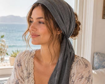 May include: A solid dark gray headscarf made of a lightweight, soft fabric. The scarf is wrapped around the head, covering the hair, with a long tail hanging down the side. The material has a subtle, fine-knit texture and a matte finish.