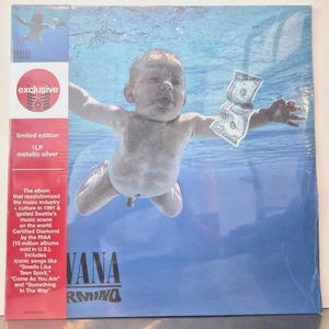 Peut inclure: Une pochette de disque vinyle Nirvana Nevermind montrant un bébé nageant sous l'eau vers un billet de dollar sur un hameçon. Le côté gauche présente une bande verticale rouge avec du texte blanc détaillant l'édition limitée 1LP argent métallisé.