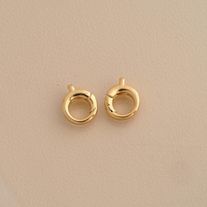 May include: Two circular gold-toned spring ring clasps, each featuring a small protruding lever mechanism for opening and closing. These jewellery findings have a smooth, polished metallic finish and a hollow centre, designed for connecting chains or charms.